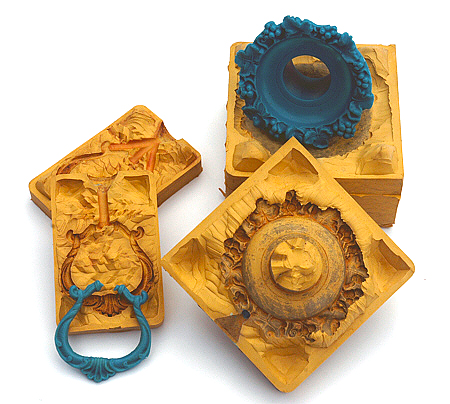 Rubber moulds of a sconce and a handle. Wax copies can be seen resting on the rubber molds